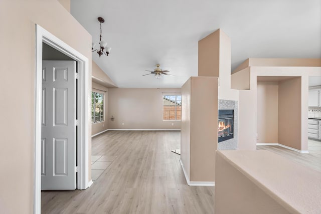 unfurnished living room featuring lofted ceiling, ceiling fan with notable chandelier, a tile fireplace, and light wood-type flooring