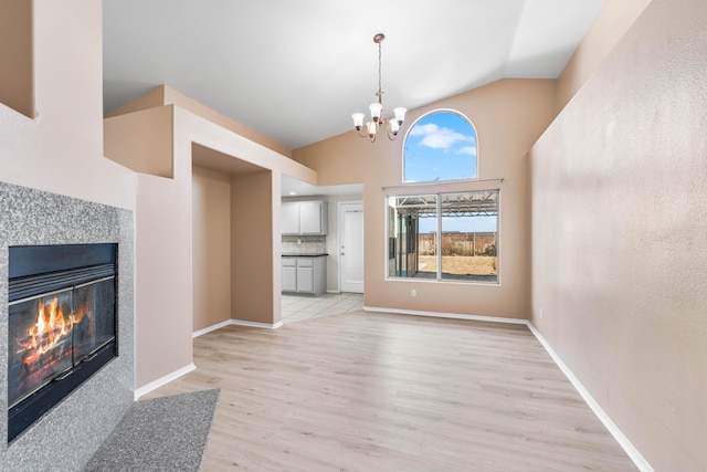 unfurnished living room with an inviting chandelier, light hardwood / wood-style flooring, and high vaulted ceiling