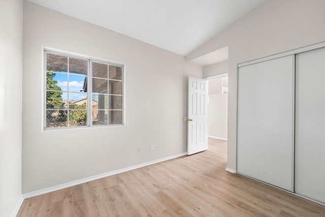 unfurnished bedroom with lofted ceiling, a closet, and light wood-type flooring