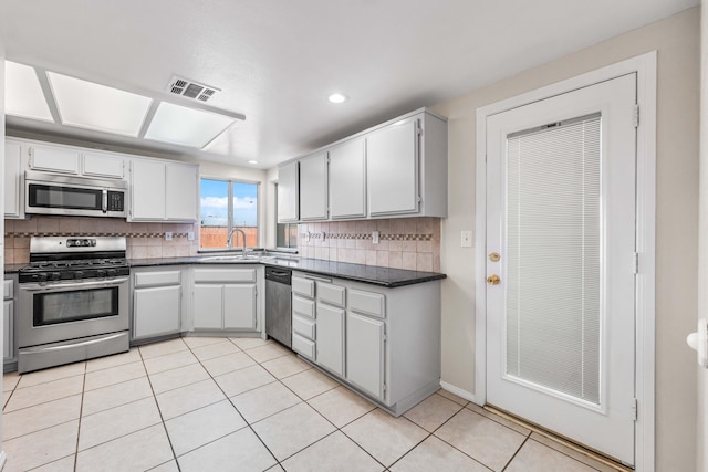 kitchen with light tile patterned flooring, appliances with stainless steel finishes, tasteful backsplash, sink, and white cabinets