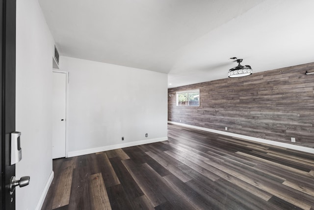 empty room with visible vents, baseboards, an accent wall, wood finished floors, and wooden walls
