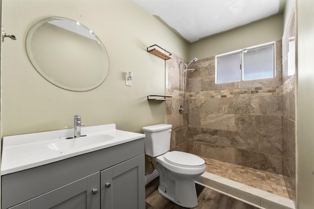 bathroom with a tile shower, toilet, vanity, and wood finished floors