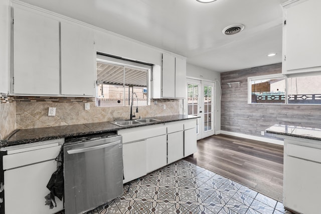 kitchen featuring stainless steel dishwasher, a sink, french doors, wood walls, and visible vents