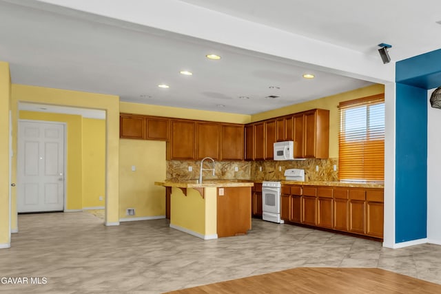 2407 Bavarian Ave, Rosamond, CA 93560 - kitchen with white appliances, decorative backsplash, brown cabinetry, a breakfast bar, and recessed lighting