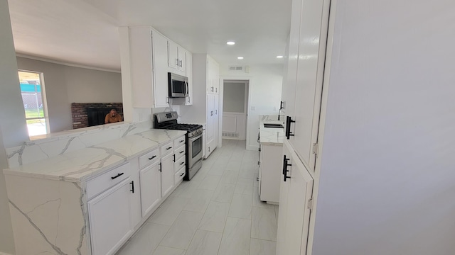 kitchen with a brick fireplace, white cabinetry, appliances with stainless steel finishes, and light stone counters