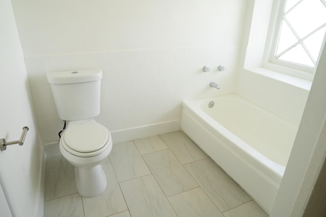 bathroom with toilet, a wainscoted wall, a bath, and tile walls