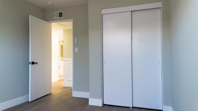 unfurnished bedroom with dark wood-style flooring, a closet, visible vents, and baseboards