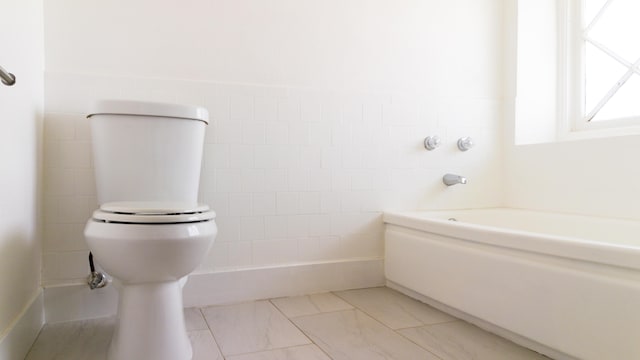 bathroom with toilet, a bath, and tile walls