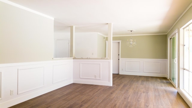 unfurnished room with an inviting chandelier, crown molding, wood finished floors, and a wainscoted wall