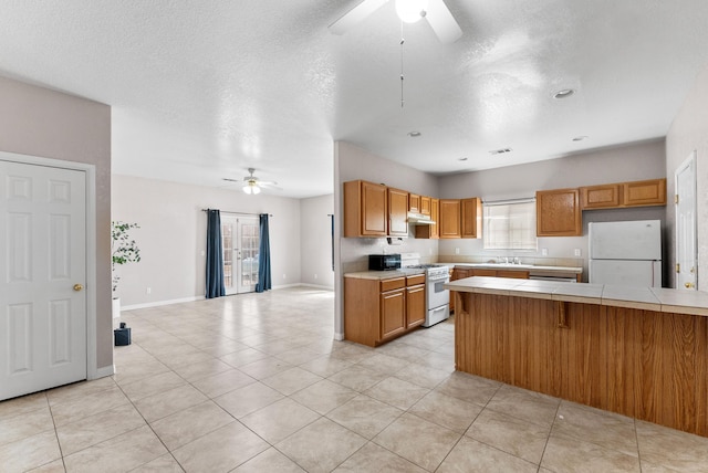 kitchen with a kitchen breakfast bar, white appliances, ceiling fan, light tile patterned floors, and tile counters