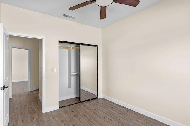 unfurnished bedroom featuring ceiling fan, a barn door, light hardwood / wood-style floors, and a closet