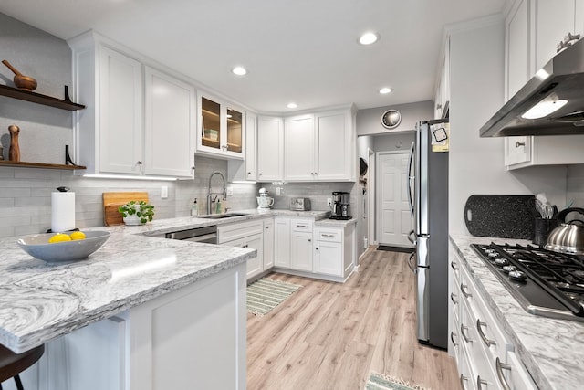 kitchen featuring light stone countertops, appliances with stainless steel finishes, sink, white cabinetry, and range hood