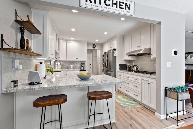 kitchen with white cabinets, a breakfast bar area, light hardwood / wood-style flooring, kitchen peninsula, and stainless steel appliances