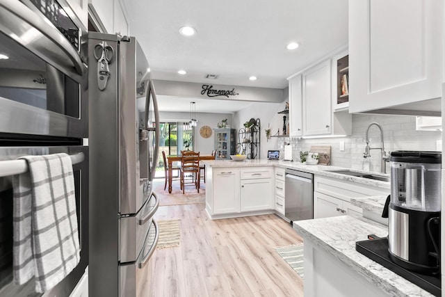 kitchen with sink, light stone countertops, appliances with stainless steel finishes, white cabinetry, and kitchen peninsula