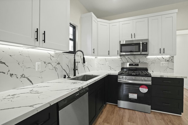 2745 Kenwood Ave, Los Angeles, CA 90007 - kitchen with white cabinets, light stone counters, stainless steel appliances, dark cabinetry, and a sink