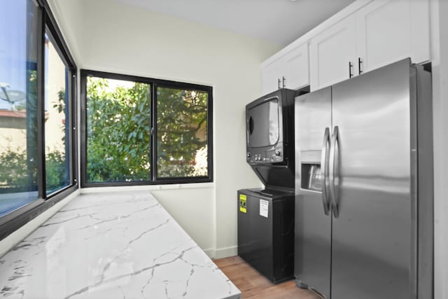 2745 Kenwood Ave, Los Angeles, CA 90007 - kitchen featuring light stone counters, stainless steel refrigerator with ice dispenser, stacked washer / drying machine, light wood-style flooring, and white cabinetry