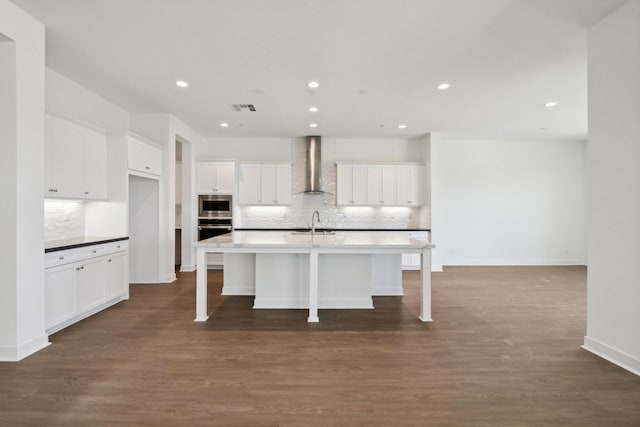 kitchen with stainless steel appliances, sink, wall chimney range hood, a center island with sink, and white cabinetry