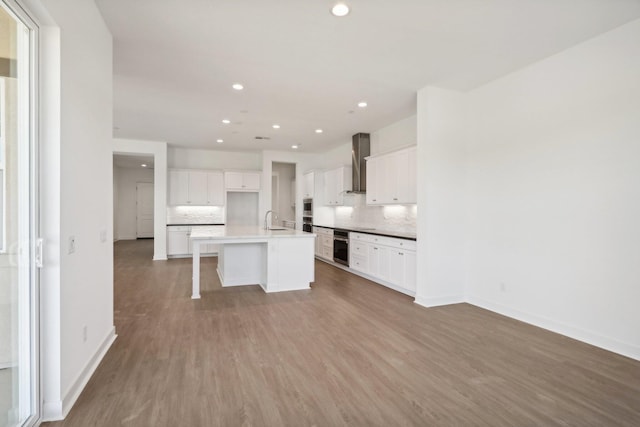 kitchen featuring white cabinetry, sink, wall chimney exhaust hood, a kitchen bar, and a center island with sink