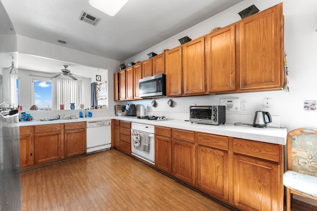 kitchen with white appliances, ceiling fan, sink, tile countertops, and light hardwood / wood-style flooring