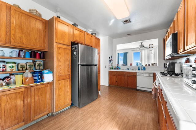 kitchen with ceiling fan, sink, tile countertops, appliances with stainless steel finishes, and light wood-type flooring