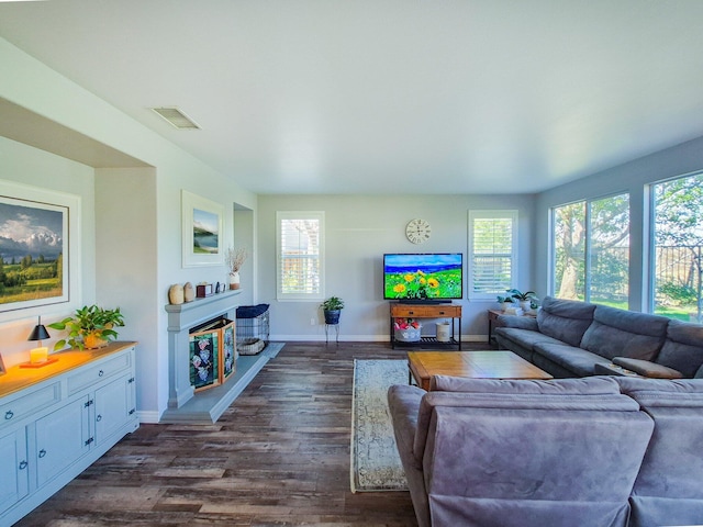 living area featuring a healthy amount of sunlight, visible vents, a fireplace with raised hearth, and dark wood-style flooring