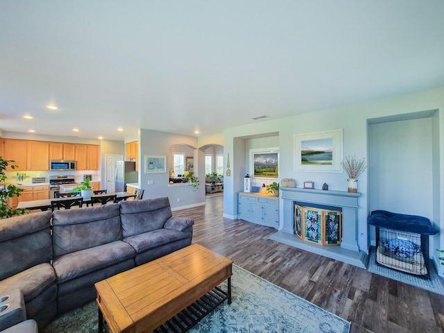 living room featuring arched walkways, recessed lighting, wood finished floors, visible vents, and baseboards