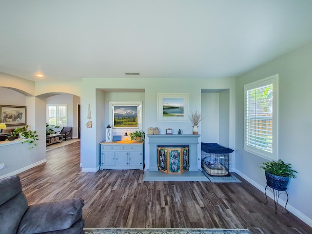 unfurnished living room featuring dark wood-type flooring, arched walkways, visible vents, and baseboards