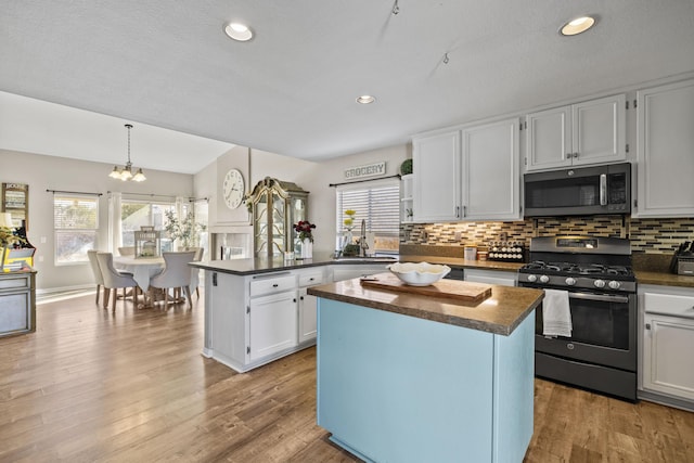 kitchen featuring gas stove, a center island, an inviting chandelier, white cabinetry, and hanging light fixtures