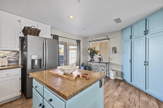 kitchen featuring a center island, stainless steel refrigerator with ice dispenser, white cabinetry, decorative backsplash, and blue cabinets