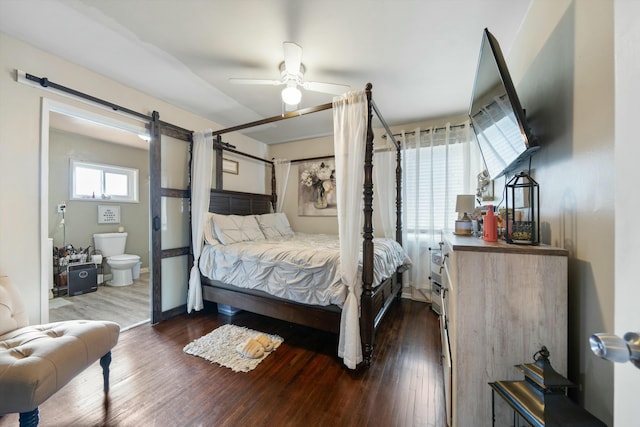 bedroom with a barn door, dark hardwood / wood-style floors, ensuite bath, and ceiling fan