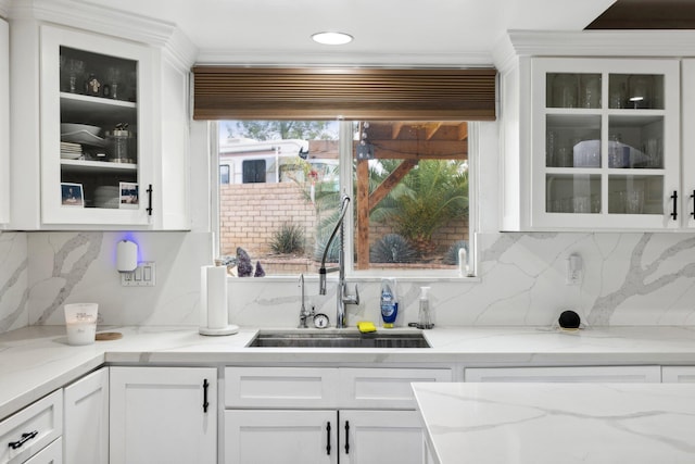 bar with backsplash, light stone counters, white cabinetry, and sink