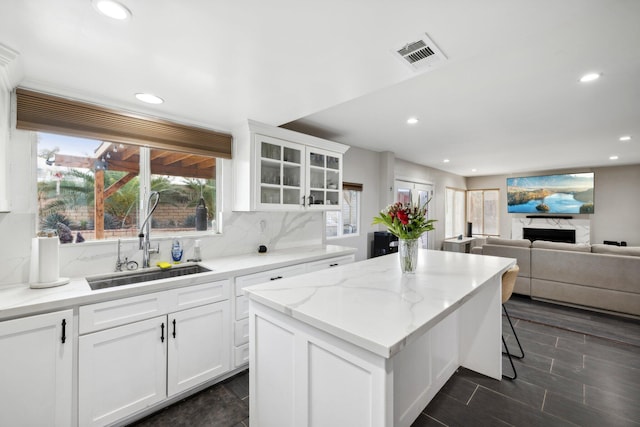 kitchen with tasteful backsplash, sink, a fireplace, a center island, and white cabinetry