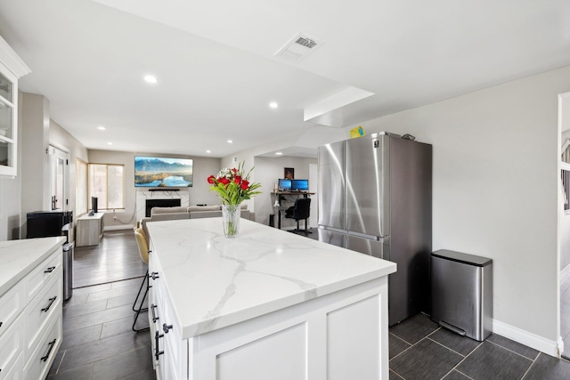 kitchen featuring light stone countertops, stainless steel fridge, white cabinetry, and a kitchen island