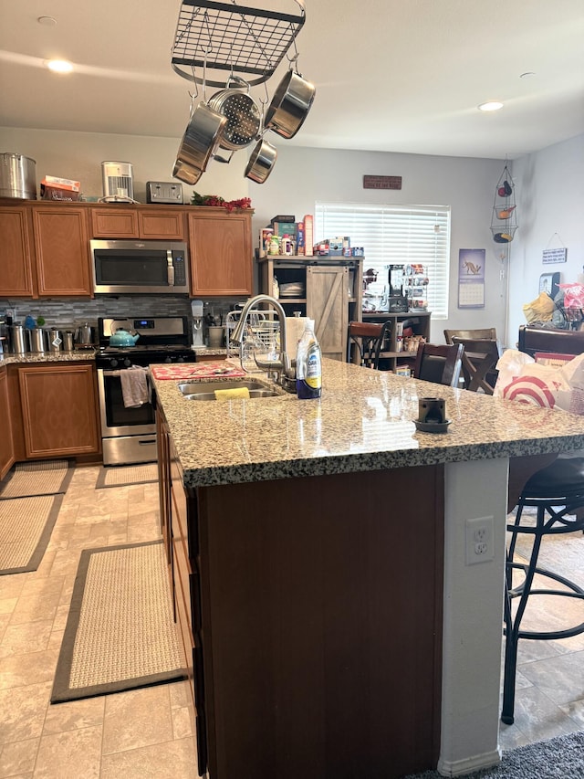 kitchen with a kitchen island with sink, stainless steel appliances, a breakfast bar, a sink, and backsplash