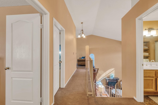 corridor featuring an upstairs landing, a sink, carpet, a chandelier, and vaulted ceiling