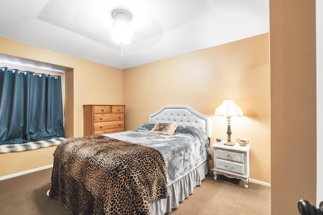 carpeted bedroom with a raised ceiling and baseboards