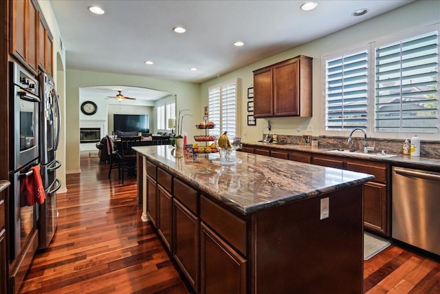 kitchen featuring sink, dark stone countertops, stainless steel appliances, dark hardwood / wood-style floors, and a center island