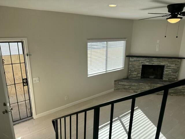 unfurnished living room featuring ceiling fan and a stone fireplace