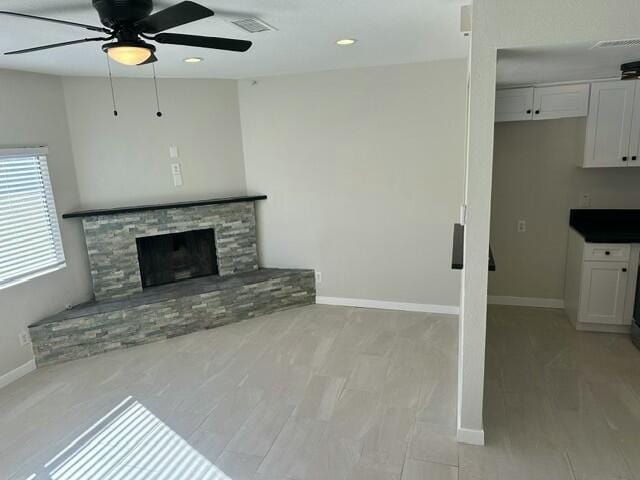 unfurnished living room with ceiling fan and a stone fireplace