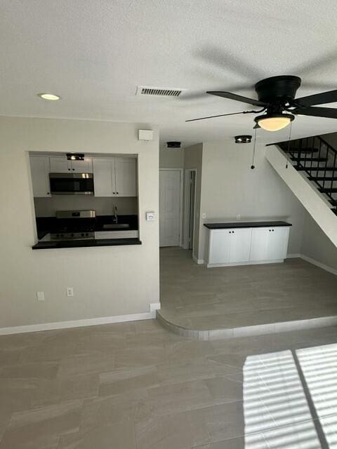 unfurnished living room featuring ceiling fan, sink, and a textured ceiling