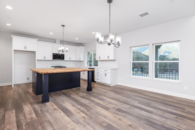 kitchen featuring white cabinets, a center island, butcher block countertops, and hanging light fixtures