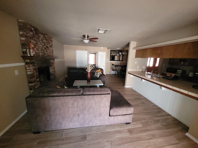 living room featuring ceiling fan, a fireplace, sink, and light wood-type flooring