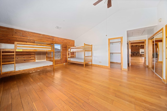 unfurnished bedroom featuring a walk in closet, wooden walls, light hardwood / wood-style flooring, a closet, and lofted ceiling