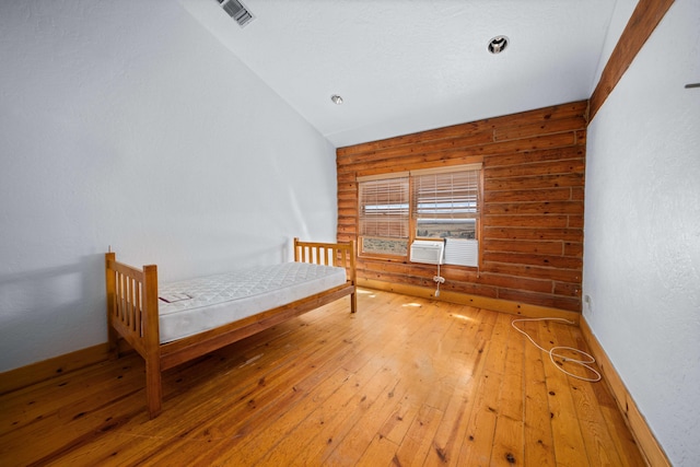 unfurnished bedroom with wooden walls, hardwood / wood-style floors, and lofted ceiling