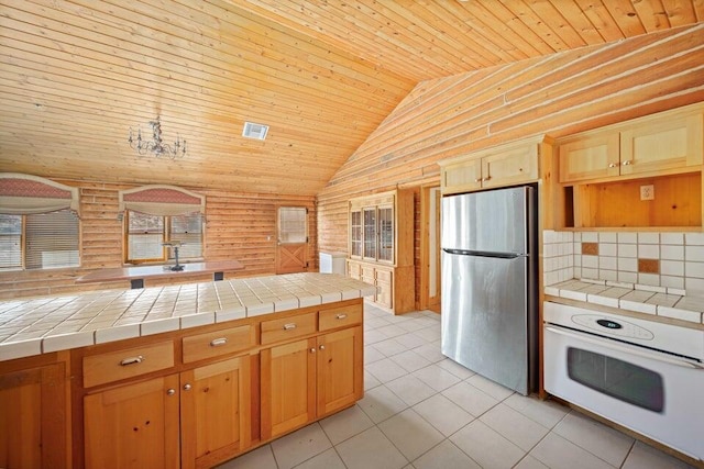 kitchen with tile countertops, oven, stainless steel fridge, and rustic walls