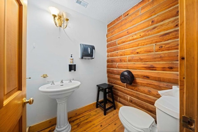 bathroom featuring a textured ceiling, toilet, rustic walls, and hardwood / wood-style floors