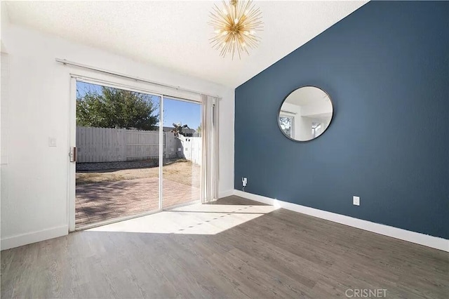 unfurnished room with an inviting chandelier, wood-type flooring, and vaulted ceiling