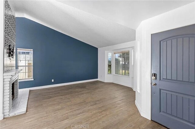 entryway with wood-type flooring, vaulted ceiling, plenty of natural light, and a brick fireplace