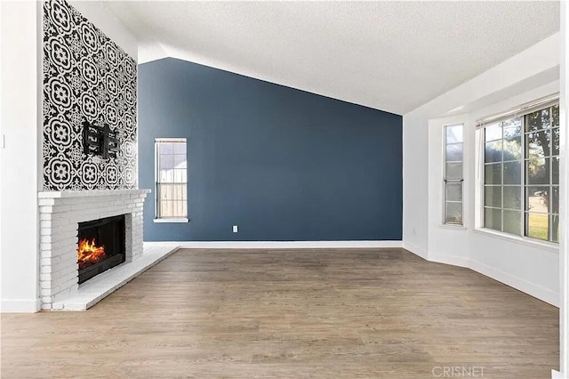 unfurnished living room featuring a textured ceiling, hardwood / wood-style flooring, a brick fireplace, and lofted ceiling