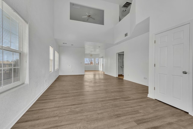 unfurnished living room with a towering ceiling, visible vents, and wood finished floors